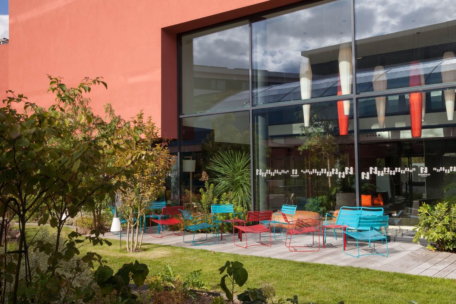 A vibrant red building surrounded by colorful chairs and tables with lively outdoor atmosphere at Nomad Hotel Paris Roissy